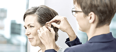 Akustikerin legt einer Kundin ein Hörgerät ans Ohr