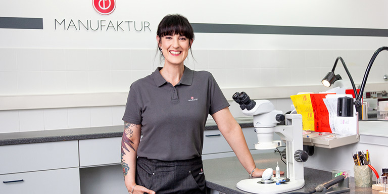 Sonja Zimmermann Teamleiterin Fertigung der Bernafon Manufaktur steht an ihrem Arbeitsplatz und lächelt in die Kamera