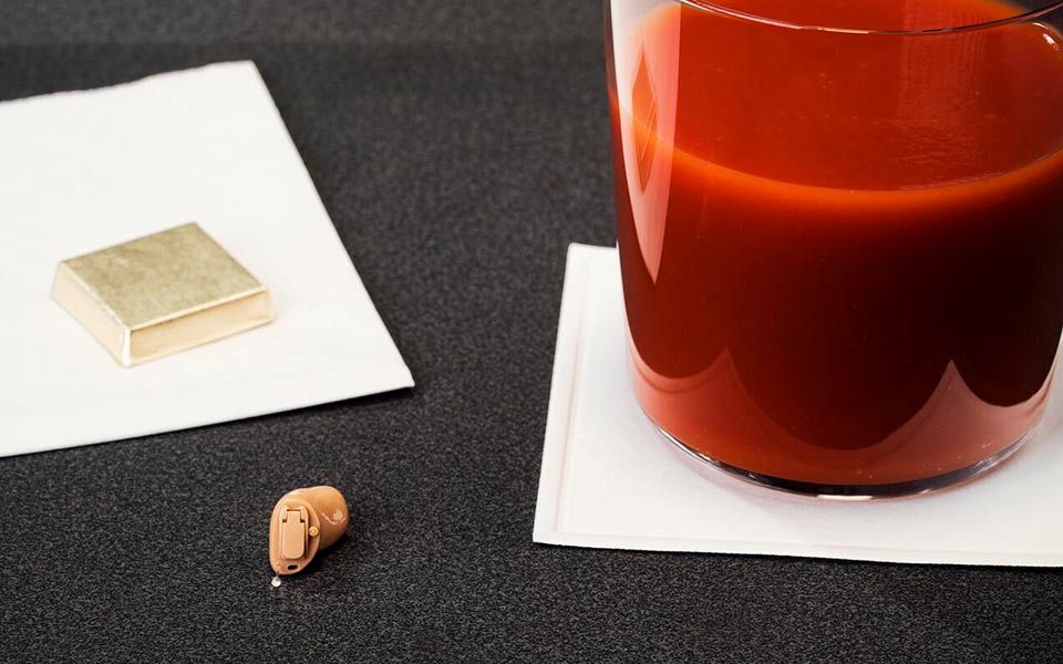Zerena Im-Ohr Hörgerät auf Tisch mit Schokolade und Tomatensaft – symbolisiert den optimalen Einsatz während eines Fluges