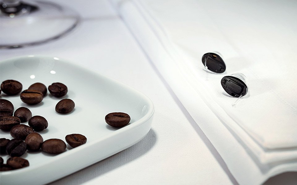 Zerena Im-Ohr Hörgeräte auf weiß eingedecktem Tisch mit Kaffeebohnen – symbolisiert den optimalen Einsatz in einem Restaurant