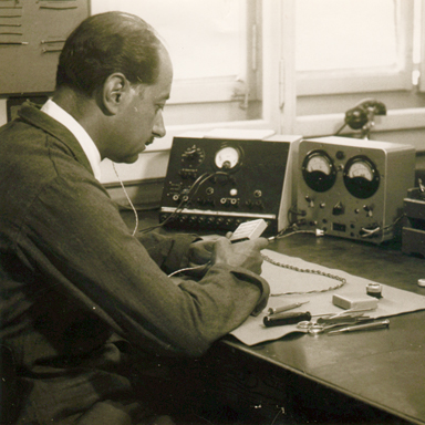 Vieille photo en noir et blanc d'un homme assis à un bureau testant des appareils auditifs Bernafon, vers 1950.