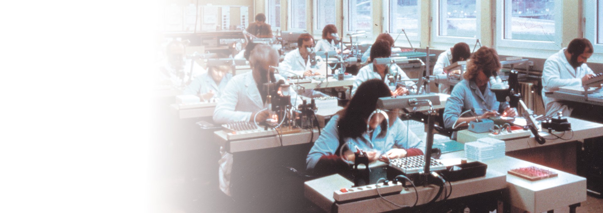 Old photo of a room full of dedicated workers in labcoats working on Bernafon hearing aid production, 1989