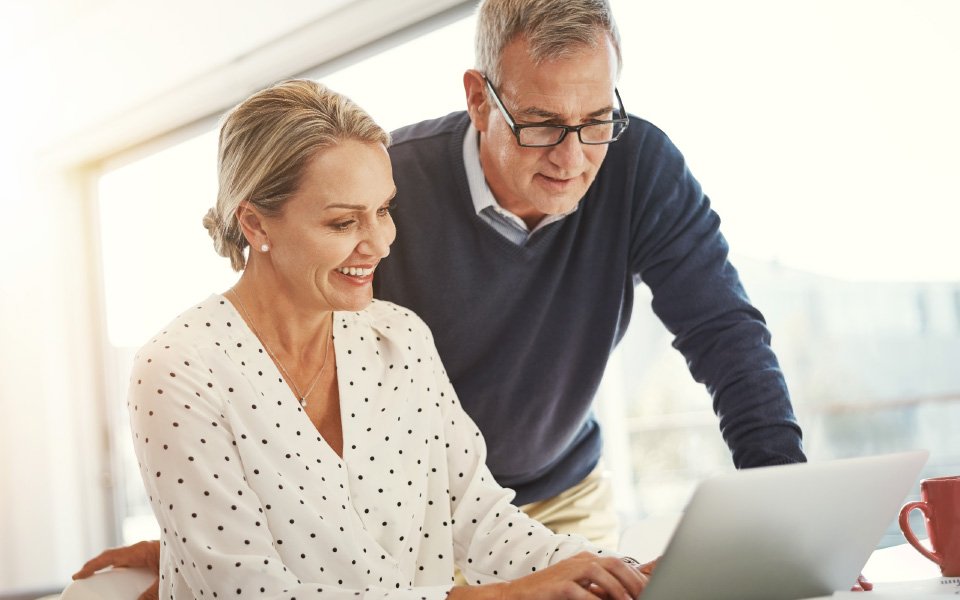 Uśmiechnięta kobieta w białej bluzce pokazująca mężczyźnie w okularach ekran laptopa