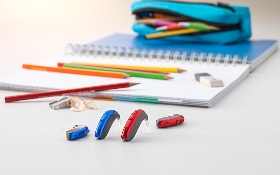 The Bernafon Leox Super Power|Ultra Power behind-the-ear hearing aids in front of colored crayons and other school materials.