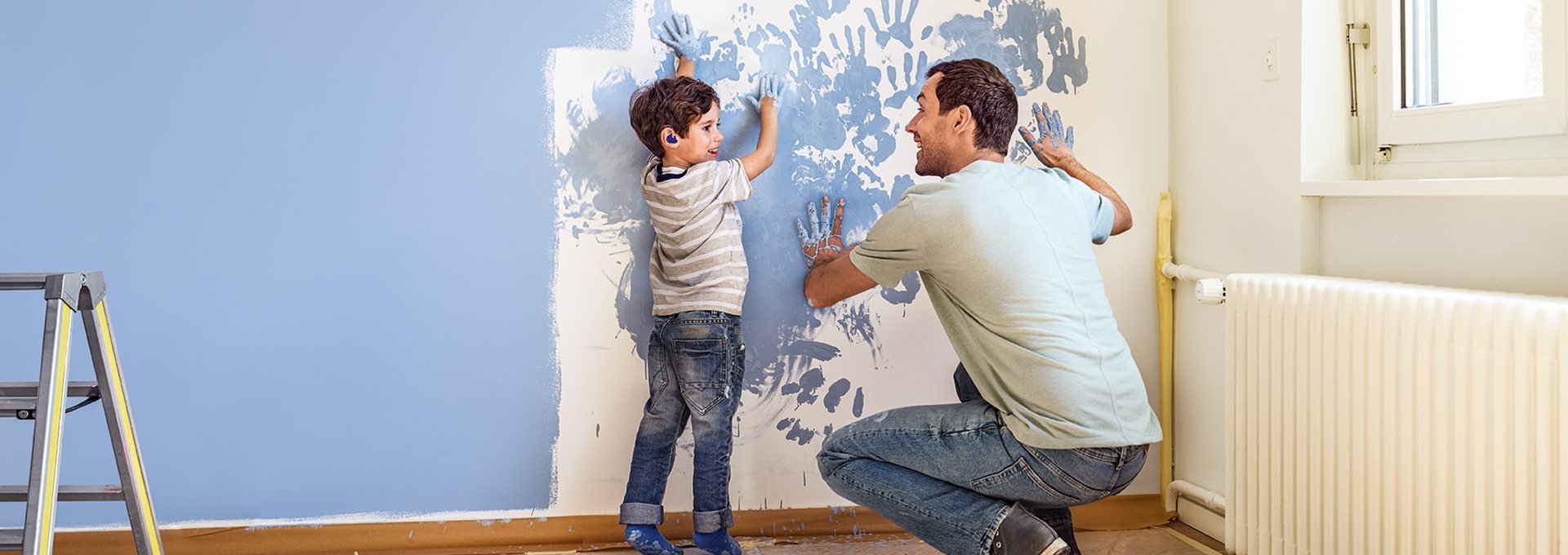 Vater und Sohn mit Bernafon Leox Super Power|Ultra Power Hörgeräten, bemalen eine Wand und fügen spontan Handabdrücke hinzu.