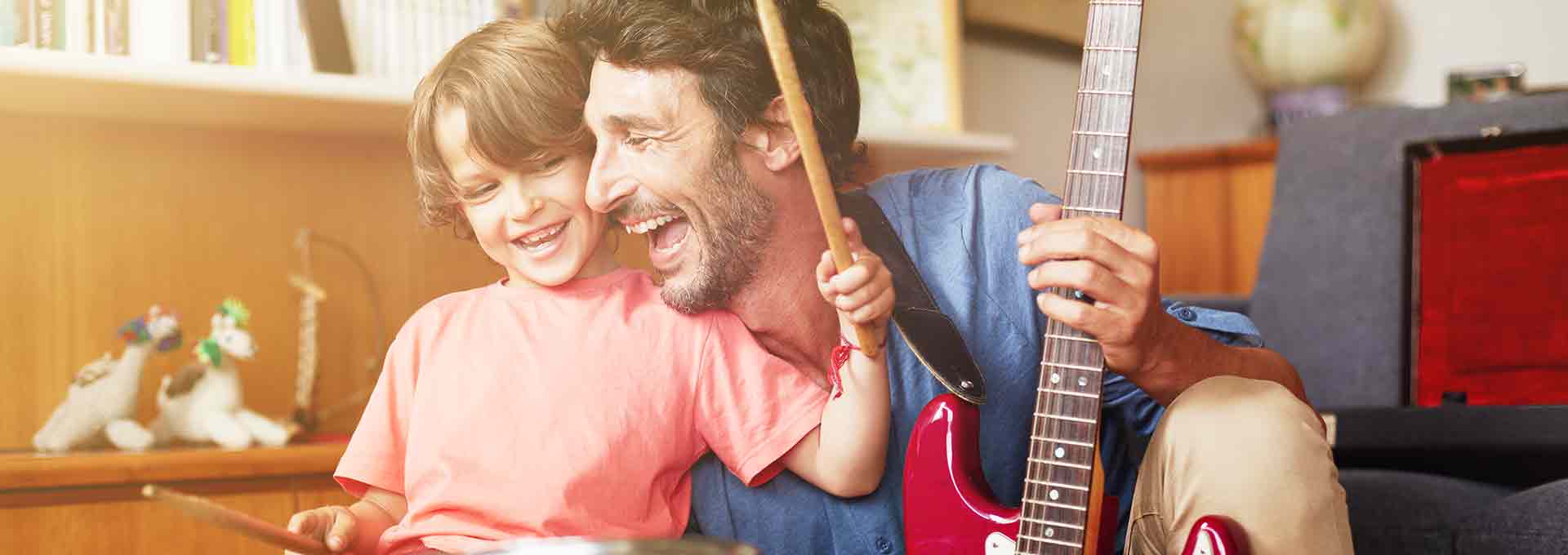 Vader met Bernafon Viron hoortoestellen speelt gitaar met zijn vijfjarige zoon die drumt en geniet van het moment.