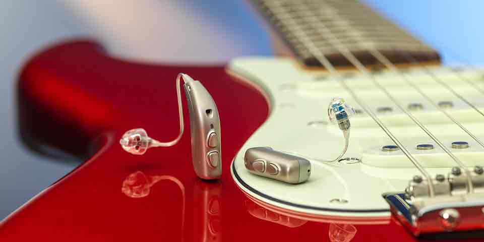 De nieuwe Bernafon Viron miniRITE T R lithium-ion oplaadbare hoortoestellen op een rode elektrische gitaar die reflecties laat zien.