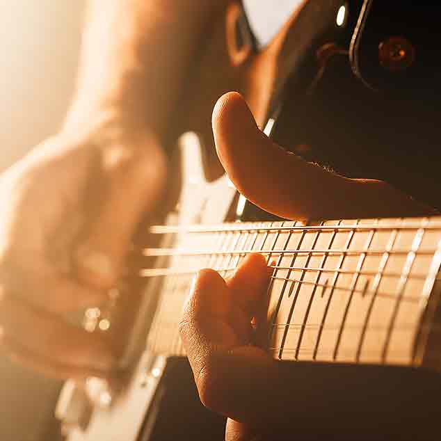 Un rockeur jouant de la guitare électronique lors d'un concert sur une scène avec de la brume et de la lumière.
