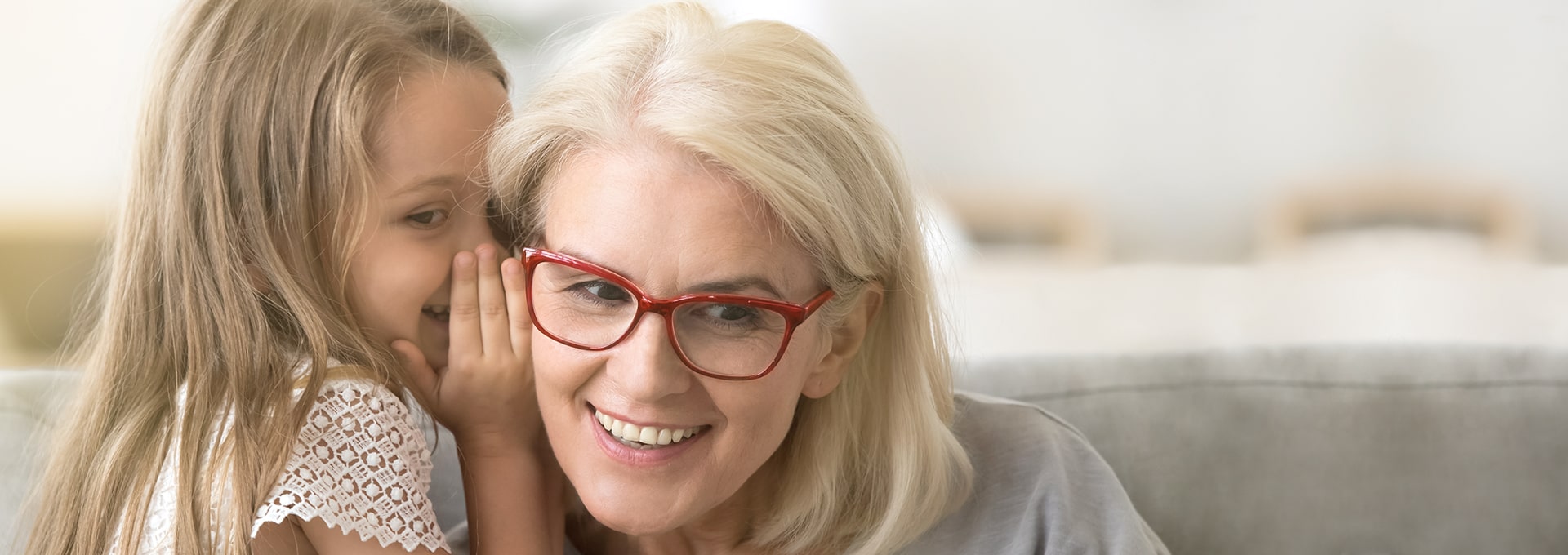 Petite fille chuchotant à l'oreille d'une femme à lunettes.