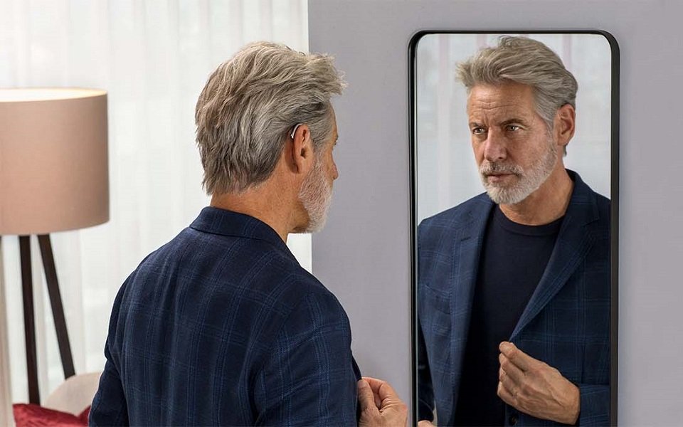Man wearing Bernafon Alpha rechargeable miniBTE T R hearing aids standing looking into a mirror, he is wearing a suit jacket