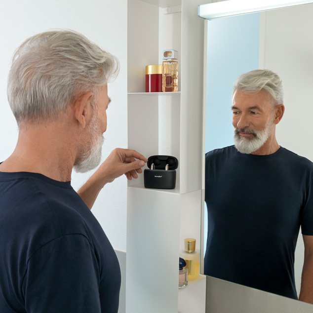 Man stands in front of bathroom mirror and removes Bernafon Alpha XT miniBTE T R hearing aids from Charger Plus