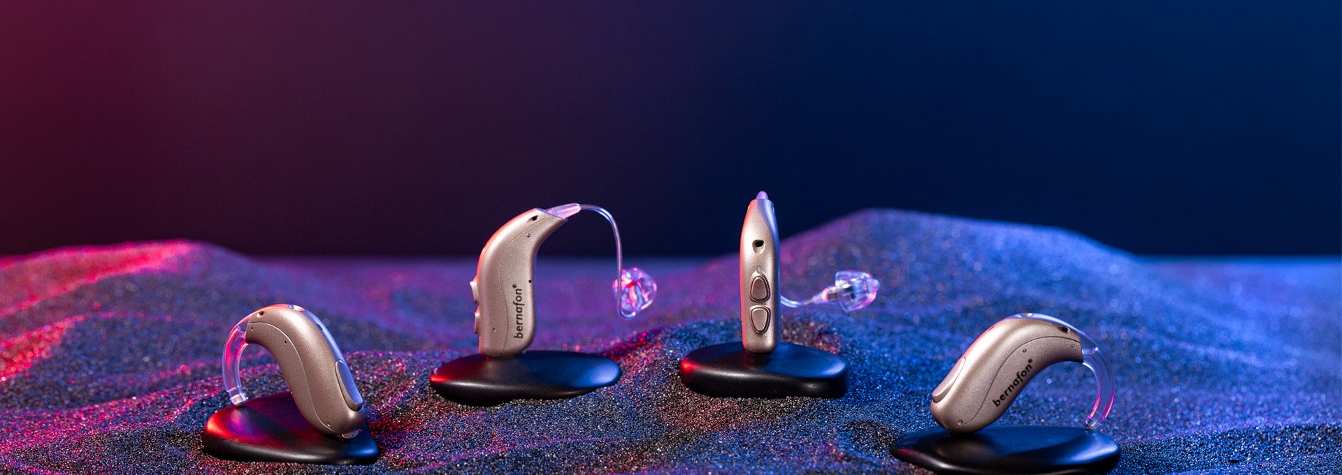 Bernafon Alpha XT miniBTE T, miniRITE T, miniRITE T R, and miniBTE T R hearing aids in black sand with red and blue lights