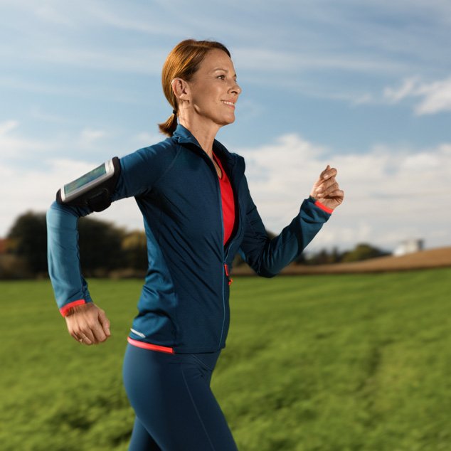 Woman wearing Bernafon Alpha XT miniRITE T R hearing aids with Hybrid Technology running outdoors next to a green field