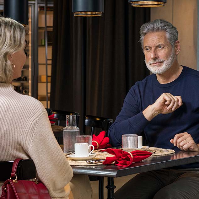 Hombre con audífonos miniBTE T R recargables de Bernafon con una mujer en un restaurante, sentados uno frente al otro