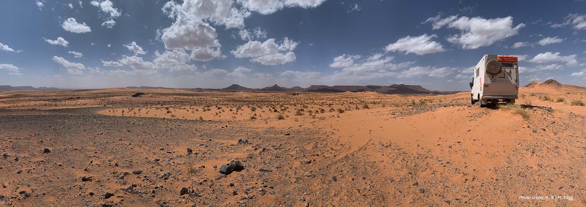 Autocaravana de los usuarios de audífonos Bernafon Alpha en el desierto con cielo azul, algunas nubes blancas y arena rojiza