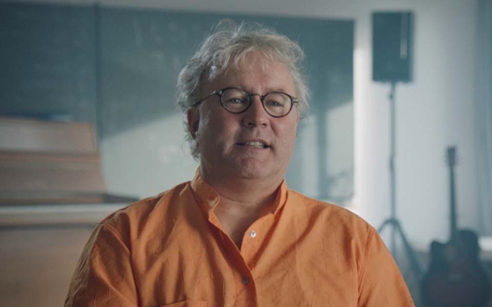 Foto de un hombre sonriente con una camisa naranja, un experimentado y feliz usuario de audífonos Bernafon Viron