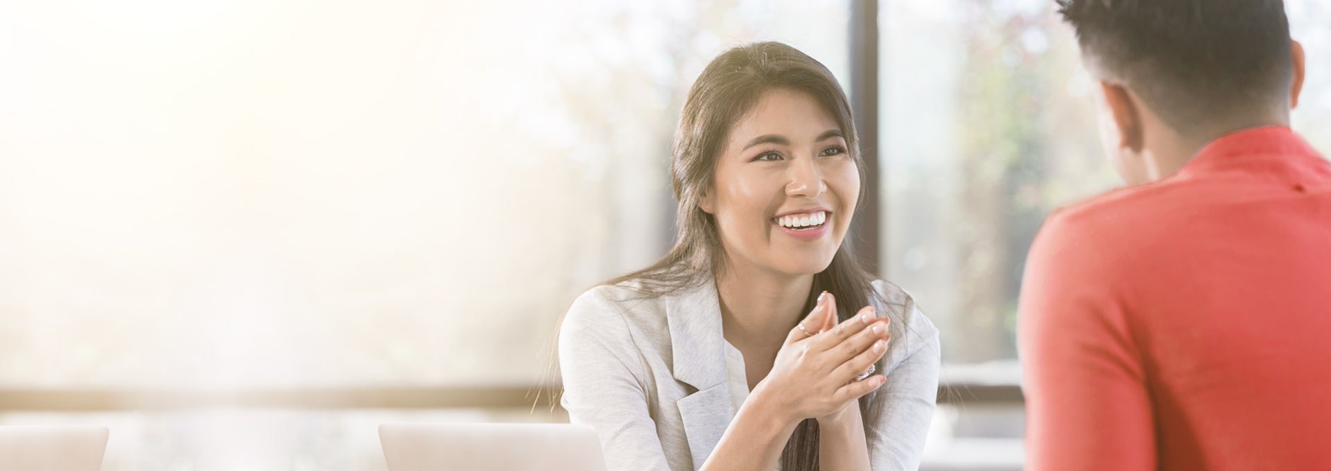 Femme d'affaires souriante, heureuse des changements positifs apportés par les appareils auditifs de Bernafon, discutant avec un client en chemise rouge.