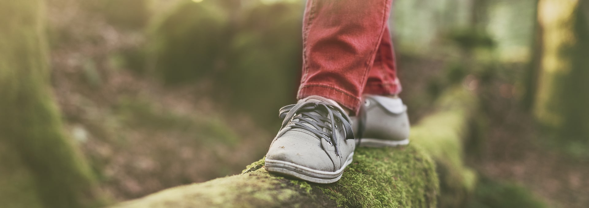 Feet wearing gray shoes balancing on a wooden log in the forest