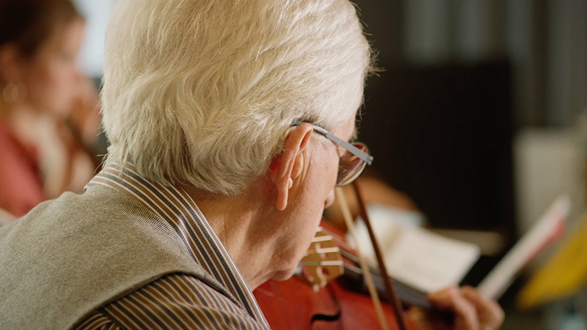 Shot of an older man playing the viola in an orchestra while enjoying the Music Experience of Bernafon Alpha hearing aids