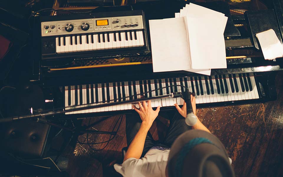 Vue du dessus d'un homme avec un chapeau jouant du piano tout en profitant de l'expérience musicale des aides auditives Bernafon Alpha.