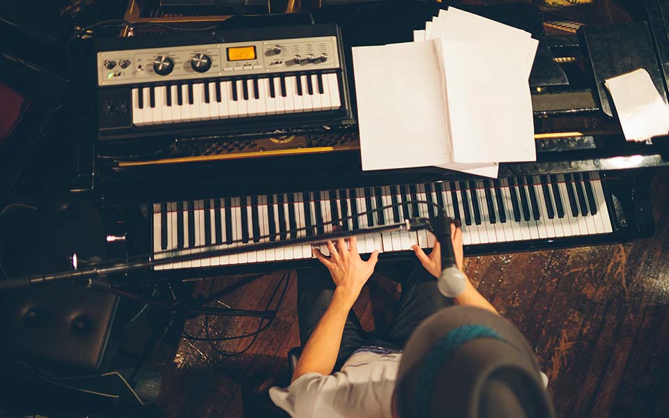 Bernafon Alpha işitme cihazlarının müzik deneyiminin keyfini çıkarırken piyano çalan şapkalı bir adamın yukarıdan çekilmiş fotoğrafı