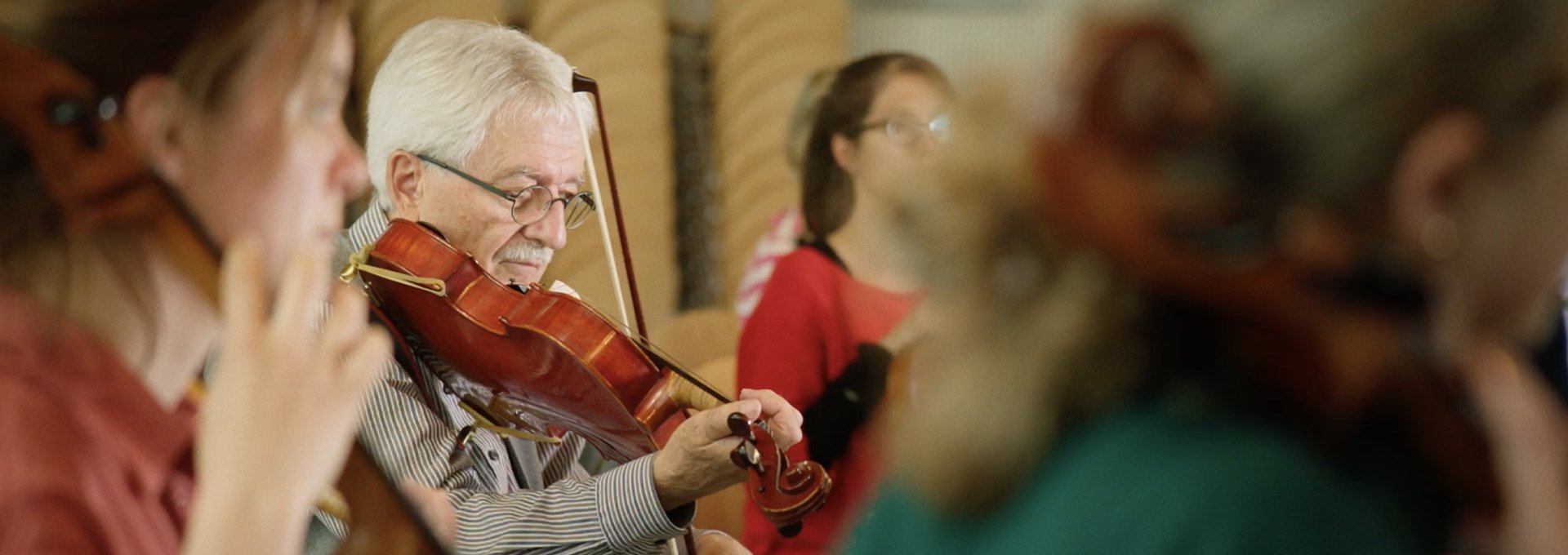 Ujęcie starszego mężczyzny grającego na altówce w orkiestrze podczas korzystania z Muzycznego Doświadczenia z aparatami słuchowymi Bernafon Alpha