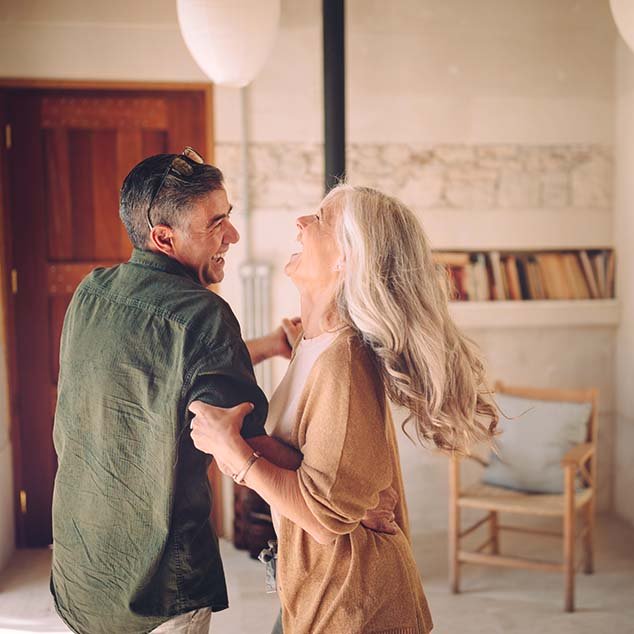 Older couple dancing and laughing at home while enjoying the Music Experience of Bernafon Alpha rechargeable hearing aids
