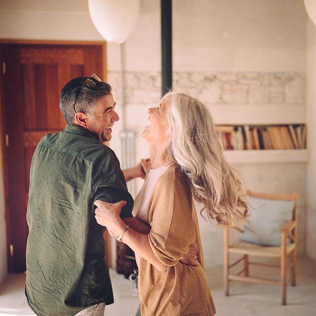 Couple âgé dansant et riant à la maison tout en profitant de l'expérience musicale des aides auditives rechargeables Bernafon Alpha.