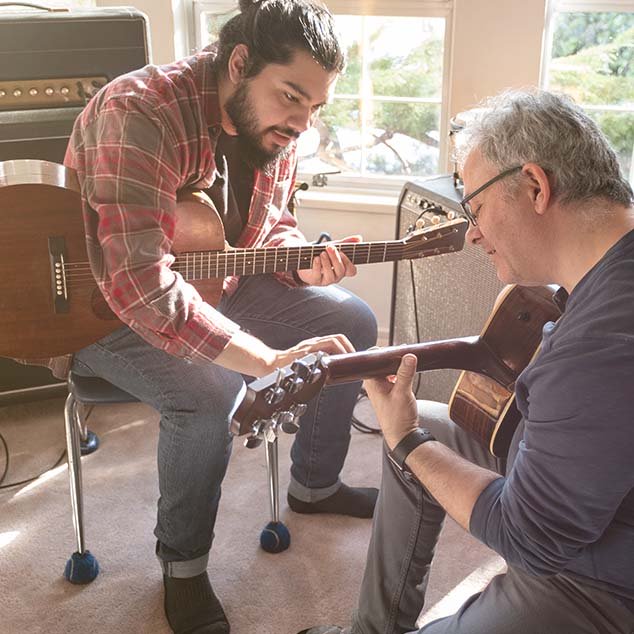 En ældre mand med genopladelige Bernafon Alpha høreapparater får guitarundervisning af en yngre lærer
