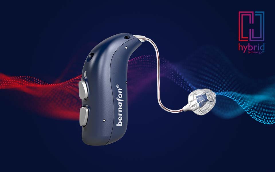 Appareil auditif rechargeable Bernafon Alpha bleu nuit avec le logo de la technologie hybride et une onde sonore rouge/bleue en arrière-plan.