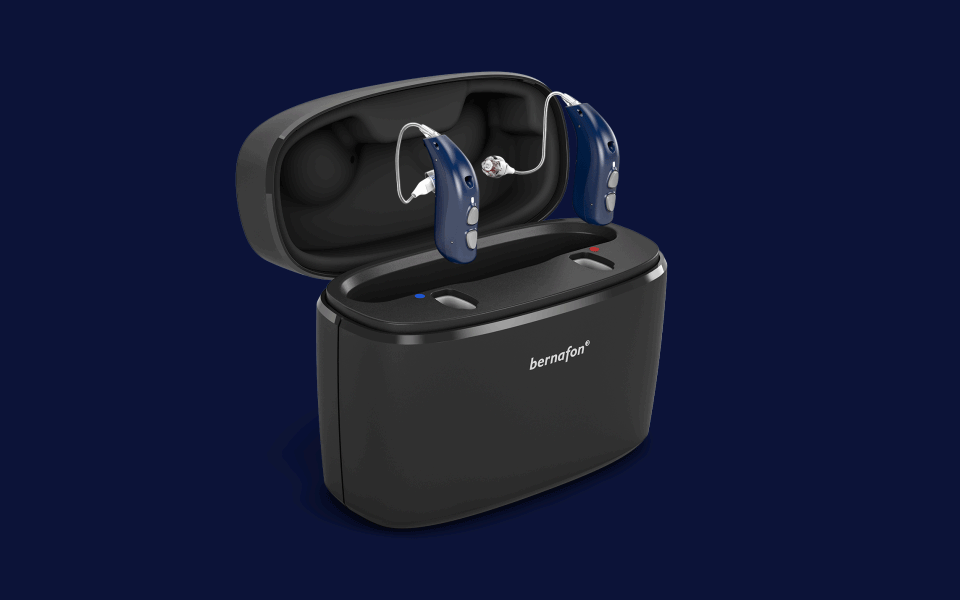 Appareils auditifs rechargeables Bernafon Alpha bleu nuit à l'intérieur du Charger Plus portable, couvercle ouvert.