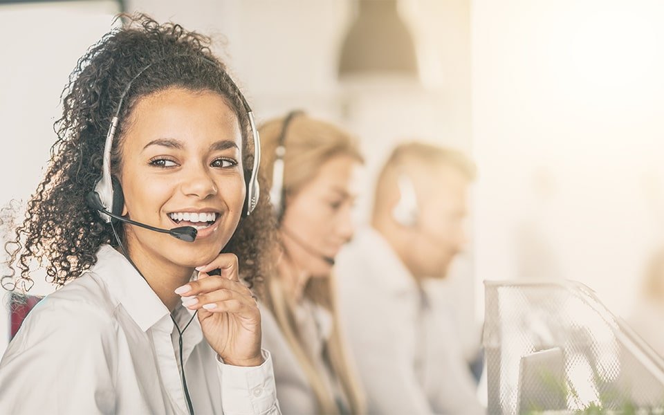 Mujer sonriente con auriculares sentada junto a dos compañeros de atención al cliente