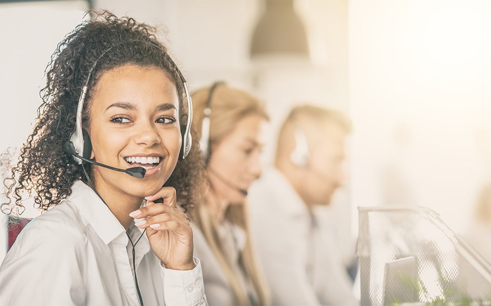 Mujer sonriente con auriculares sentada junto a dos compañeros de atención al cliente