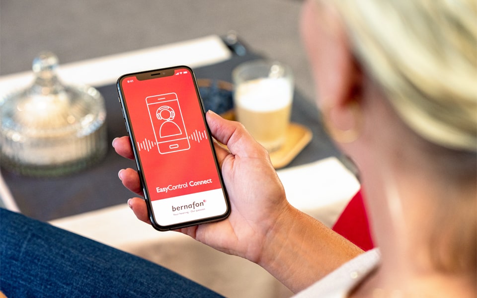 Femme blonde tenant son téléphone avec l'écran de démarrage de l'application Bernafon.