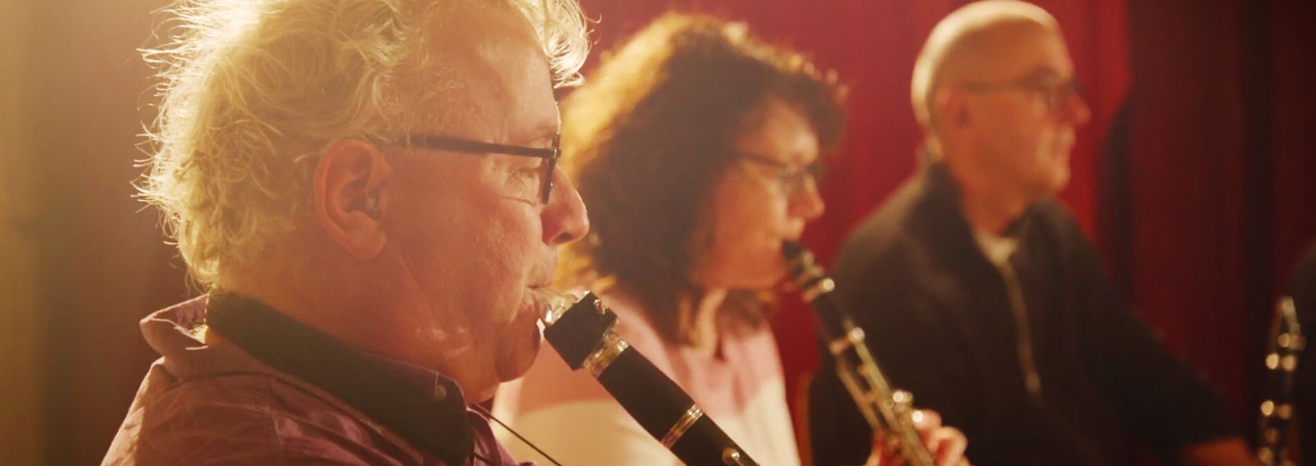 A music teacher with hearing aids directing a school band with trumpet players, and more students playing music