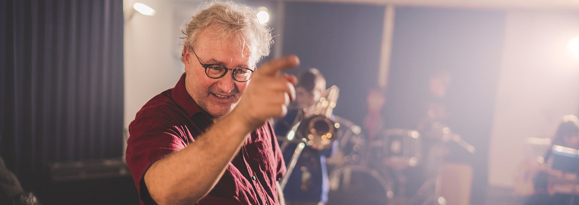 Un professeur de musique équipé d'appareils auditifs dirige un orchestre scolaire avec un trompettiste, un batteur et d'autres élèves jouant de la musique.