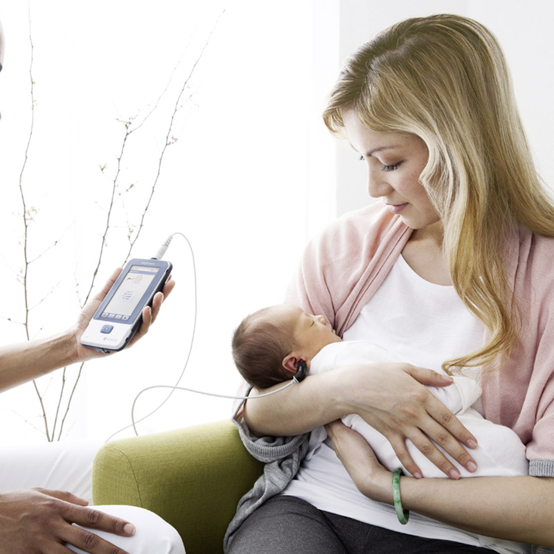 A mother holding her baby while doctor is performing a screening with a MAICO easyScreen
