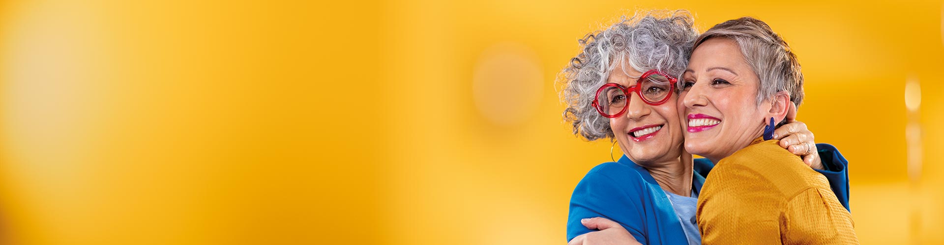 Two middle-aged women hugging each other. One is wearing Philips HearLink in-the-ear almost invisible hearing aids.