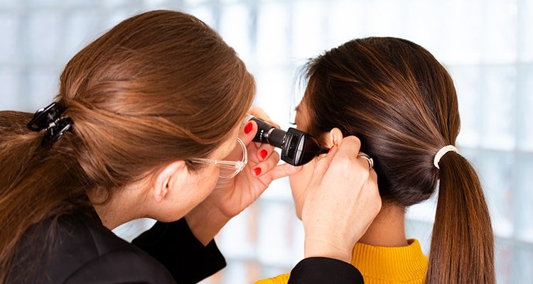 A female audiologist looks into a young woman’s ear with an otoscope to seek causes of hearing loss.