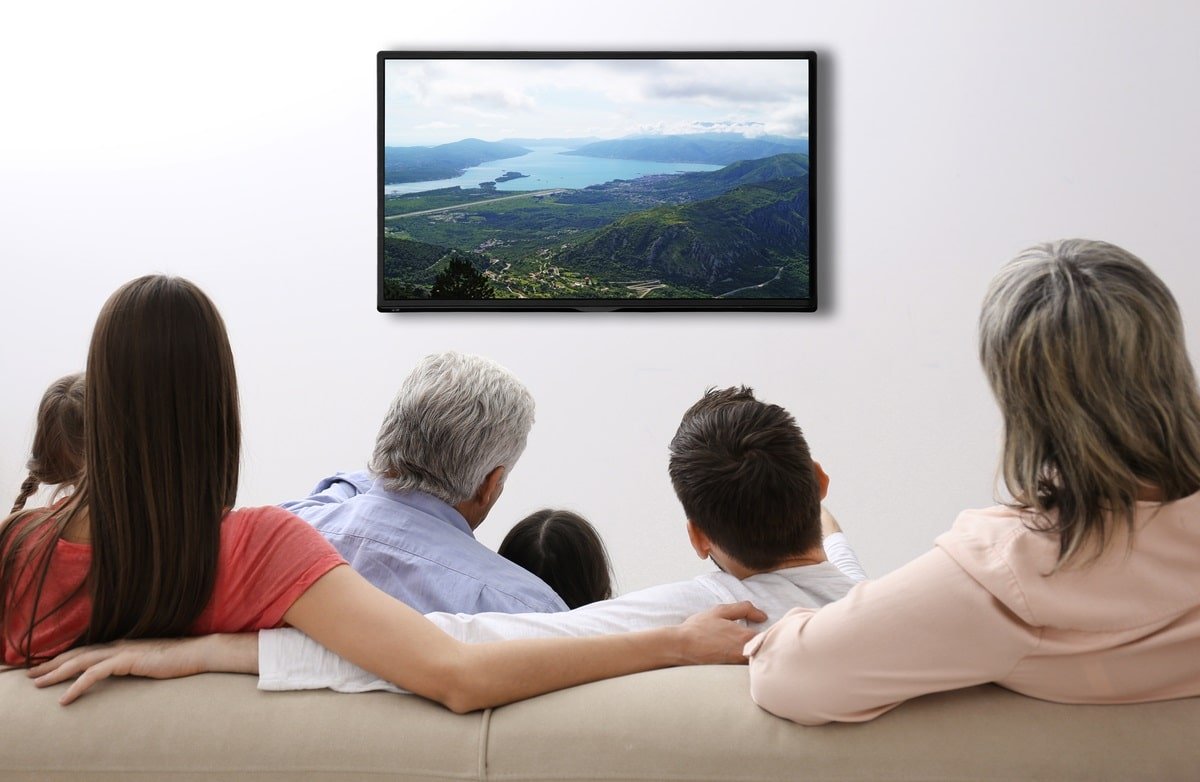 Une familles assise sur un canapé regard un écran de télévision