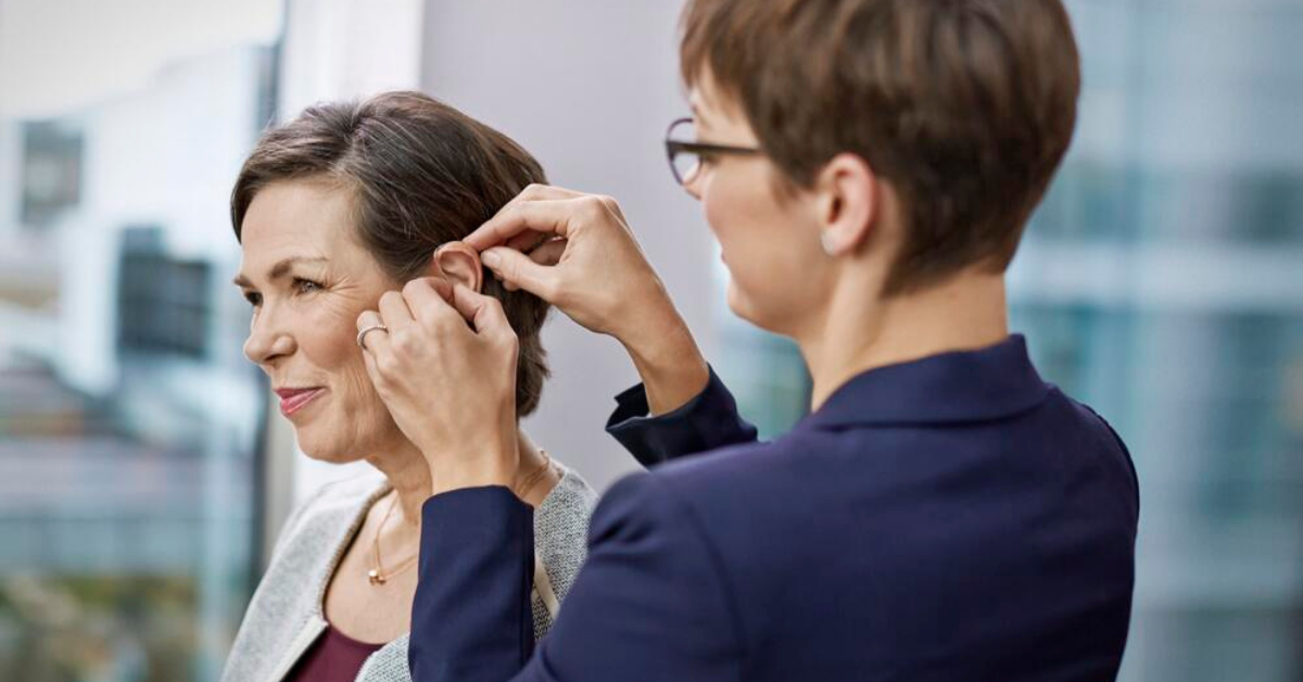 Une femme audioprothésiste pose un appareil auditif sur l'oreille d'une femme