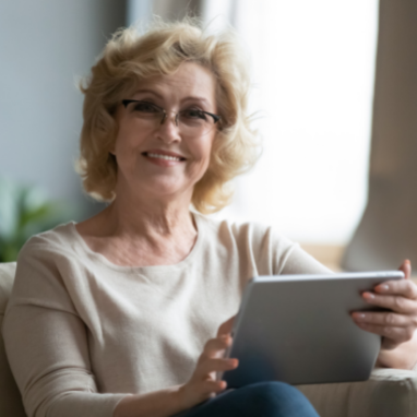 Une femme souriante est assise avec une tablette à la main