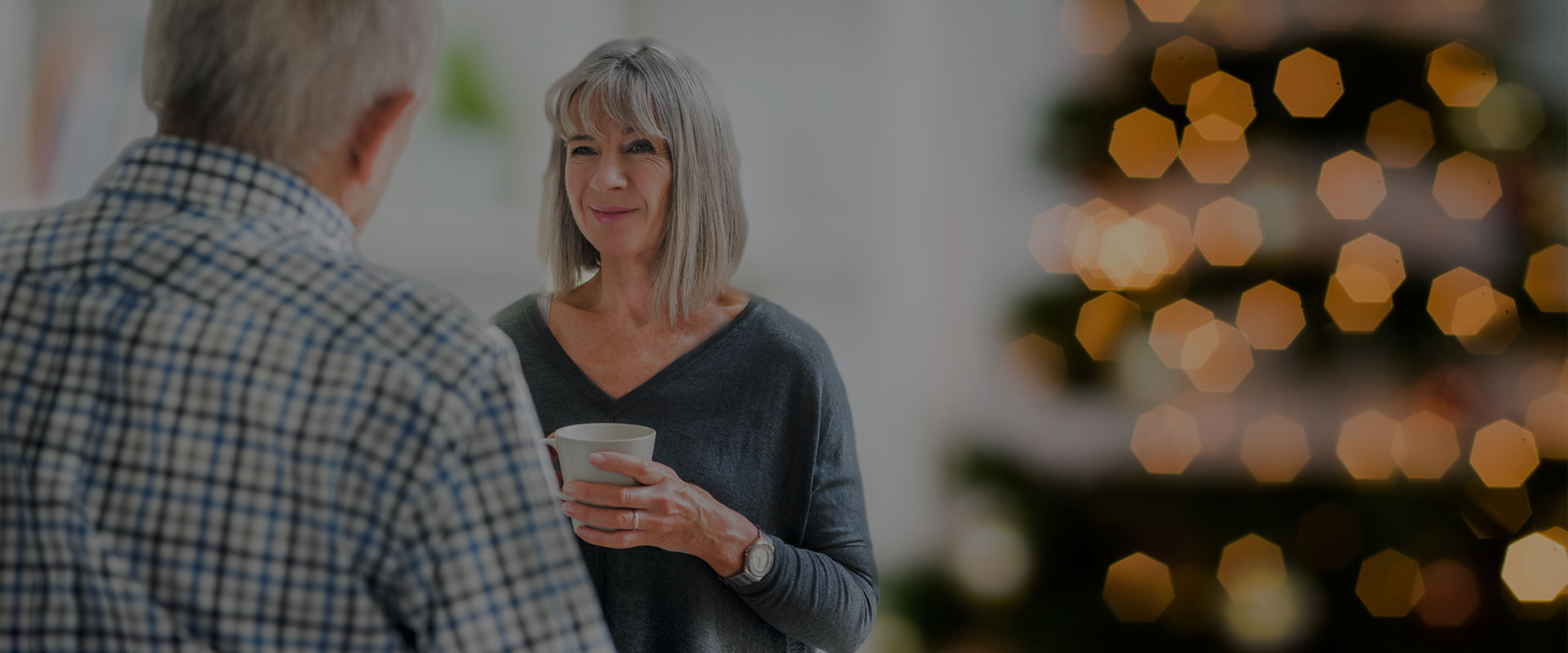 deux personnes un homme et un femme tenant un thé dans ses mains parlent devant un sapin de Noël