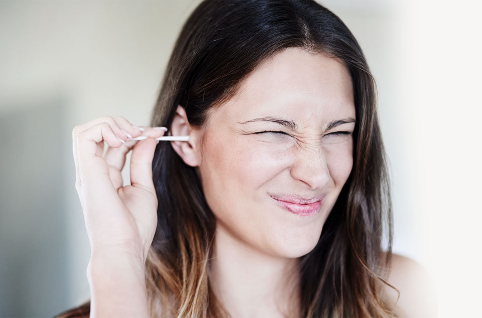 jeune femme se nettoyant les oreilles avec un coton tige en faisant la grimace