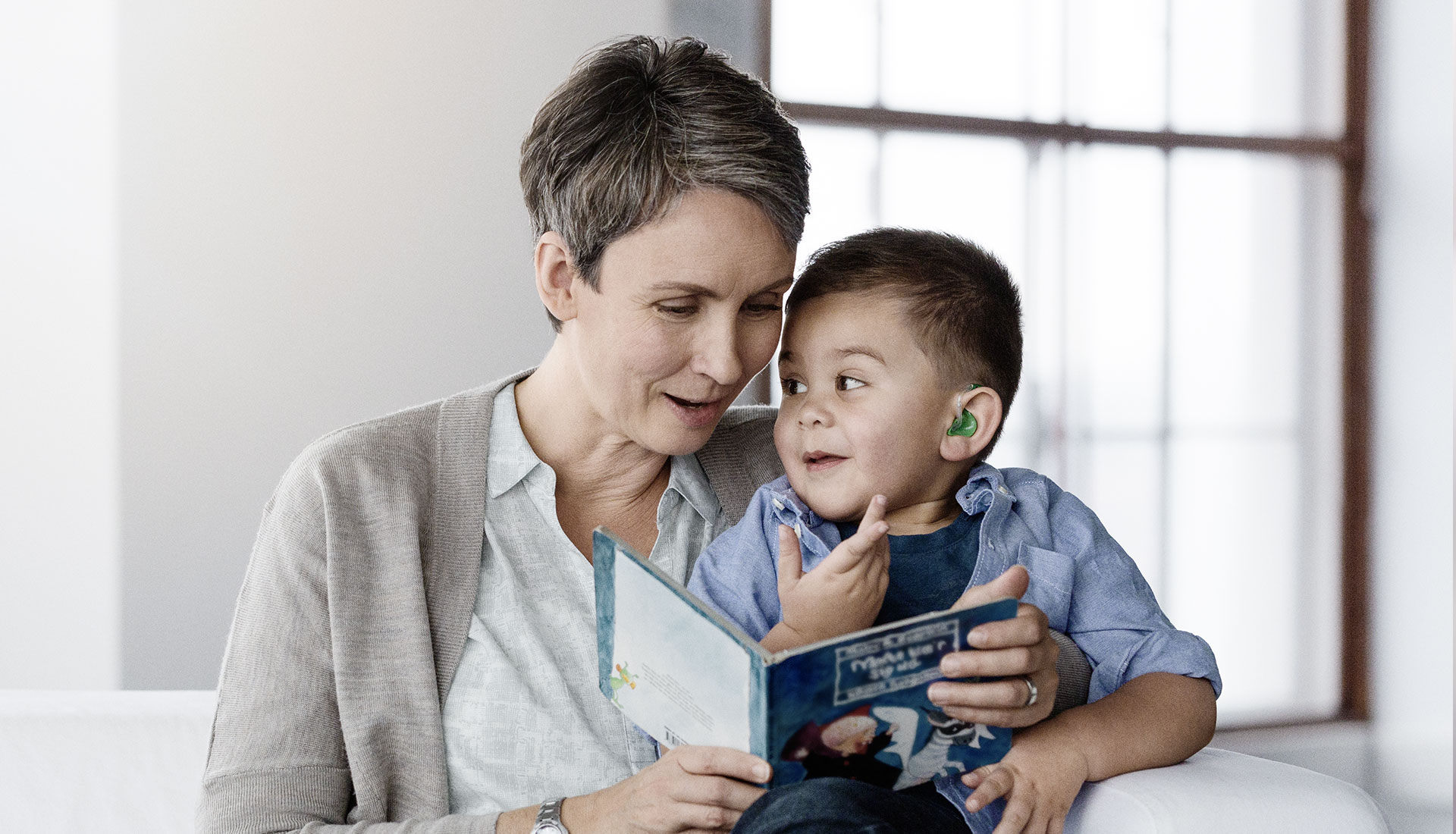 Femme et petit garçon portant un appareil auditif lisent un livre d'histoires