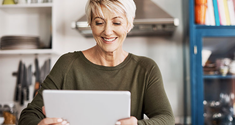 Frau in den Fünfzigern, die einen Online-Hörtest auf ihrem Tablett macht, während sie zu Hause ist.