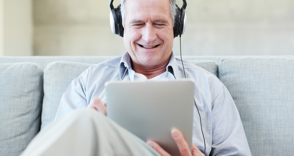 Mann sitzt auf der Couch und prüft sein Gehör mit den Online-Hörtest.