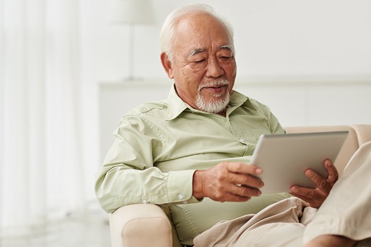 Mann sitzt auf einer Couch und sucht auf seinem Tablet nach Philips HearLink Hörgeräten