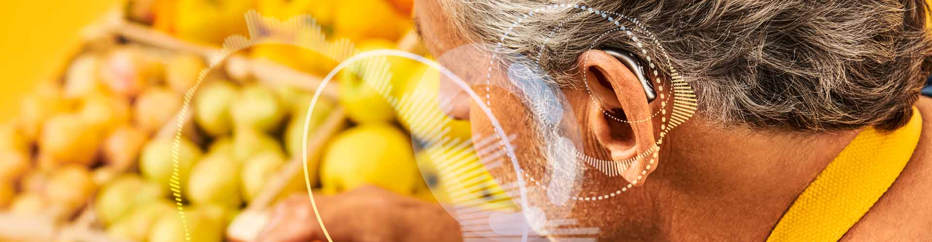 Man wears Philips HearLink rechargeable miniRITE T R hearing aids while arranging oranges in his sustainable farmer's market stand