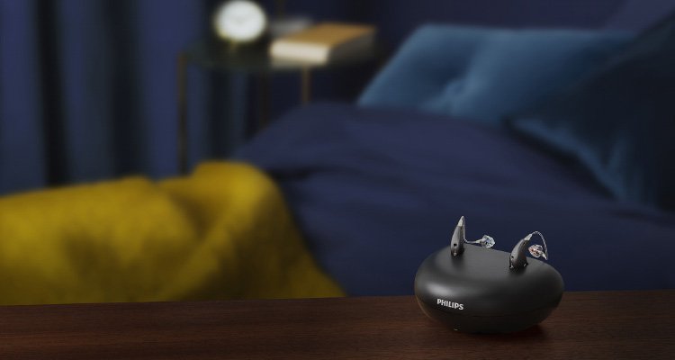 Philips HearLink miniRITE T R rechargeable hearing aids in the charger on a table in a bedroom. 